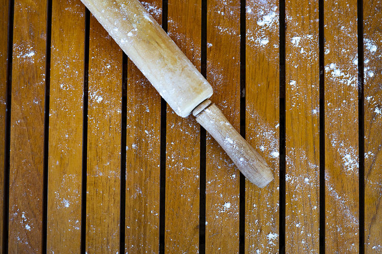 Wooden rolling pin with flour on a wooden background.