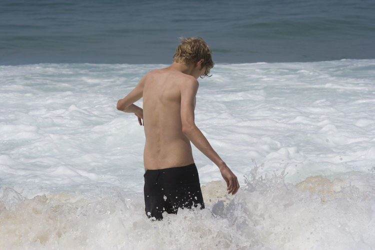 Rear view of shirtless teenage boy walking in sea