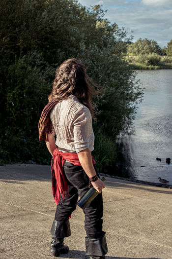 Rear view of man with long hair standing by water dressed as a pirate.