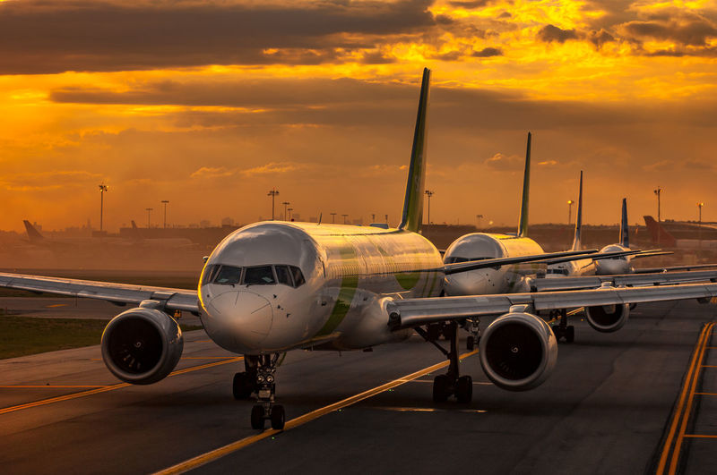 Airplane on airport runway against sky during sunset
