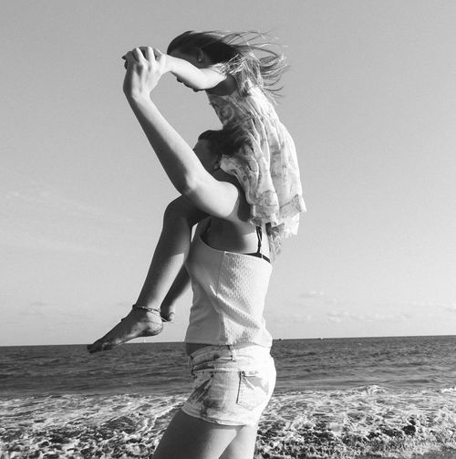 Side view of woman carrying daughter on shoulder at beach