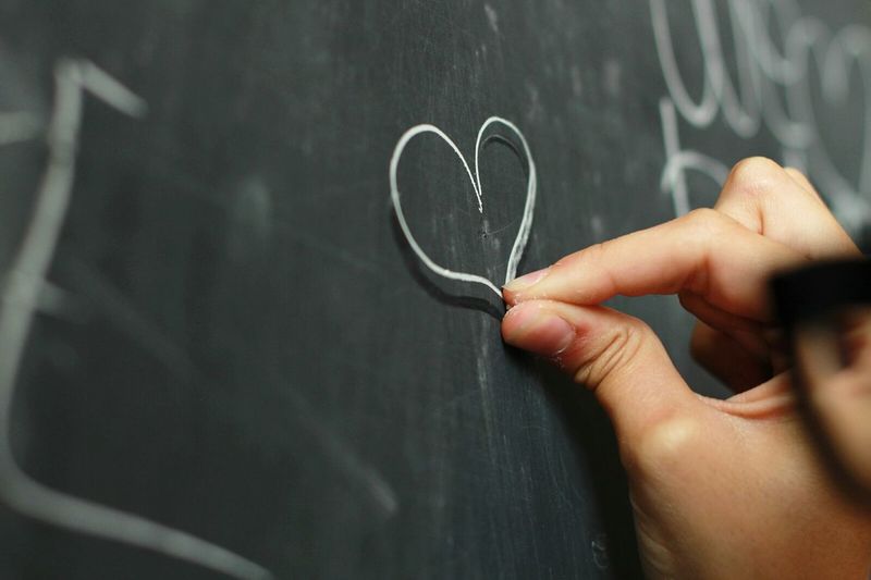 Cropped hand of person drawing heart shape on blackboard