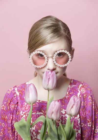 Mod tween girl smelling pink tulips against pink backdrop, portrait