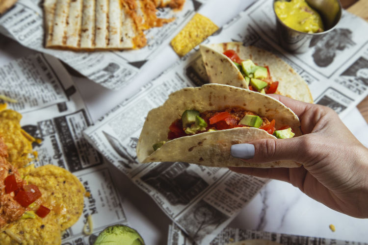 Female hands hold mexican beef tacos with vegetables on restaurant table. top view person