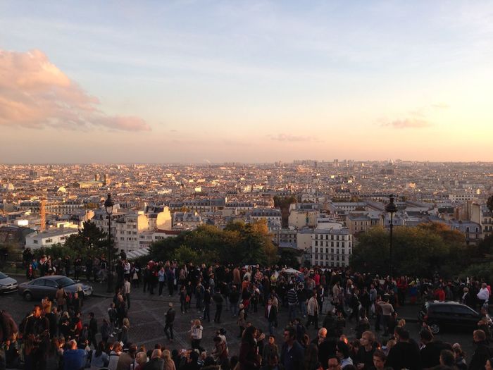 Crowd by cityscape against sky during sunset at saint-ouen