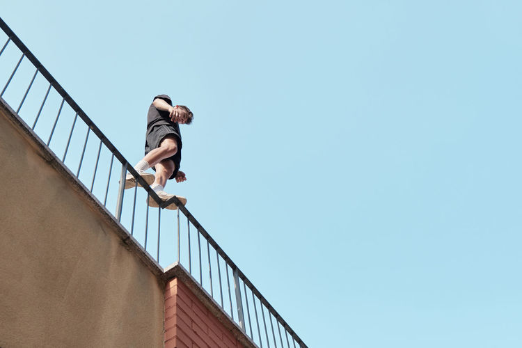 From below of male standing on metal railing of building and preparing for performing parkour trick