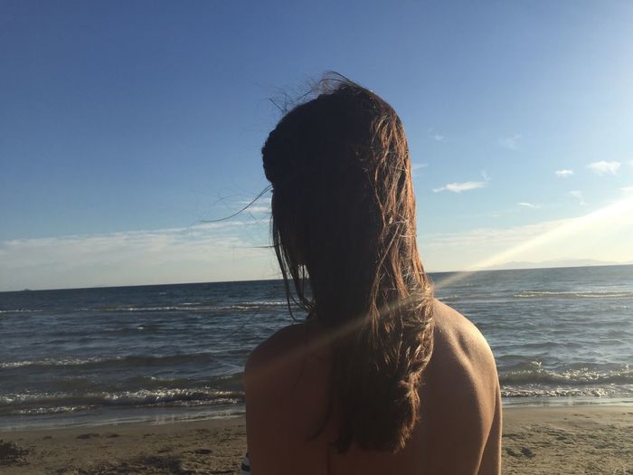 Rear view of shirtless woman at beach against sky