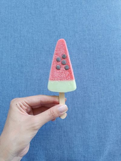 Close-up of hand holding ice cream against blue wall