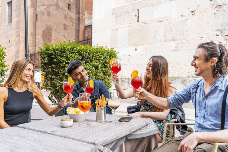 Smiling friends toasting drinks while sitting at cafe