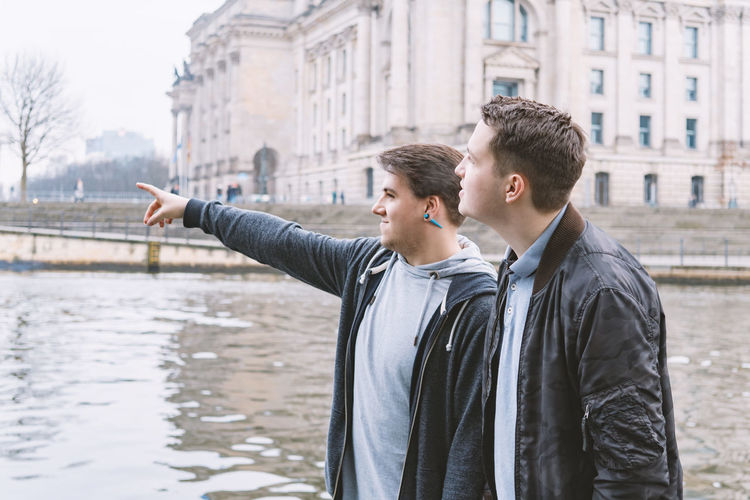 Man pointing with friend while standing at riverbank in city
