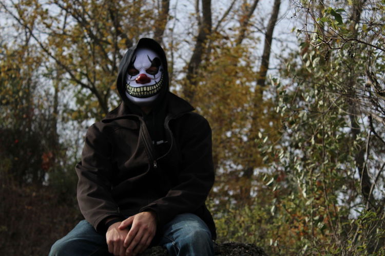 Man wearing scary clown mask against trees