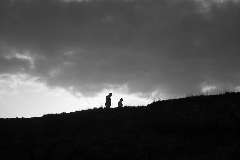 Silhouette people walking on landscape against sky during sunset