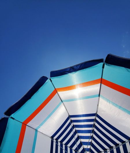 Low angle view of parasol against clear blue sky
