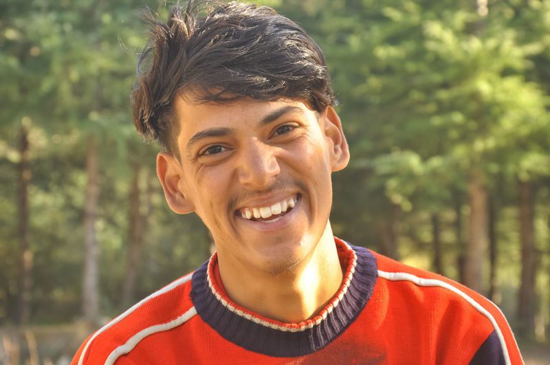 Portrait of smiling south asian young man  sitting against trees