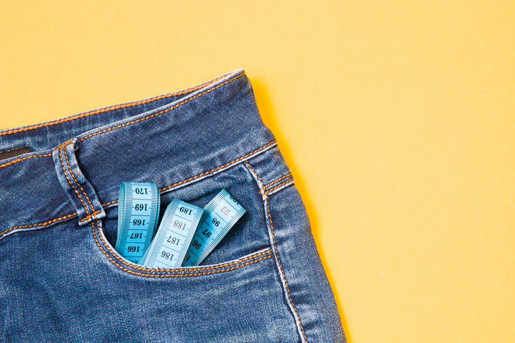 Close-up of jeans with tape measures over colored background