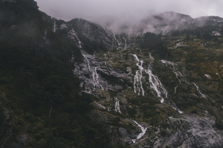Waterfalls down a mountain into milford sound, foggy and rainy day, nz