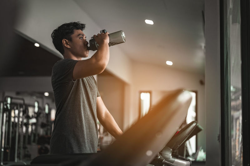 Young man drinking water while exercising in gym