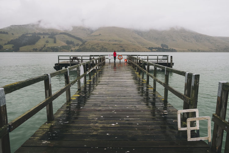 Woman on a red jacket standing at port levy jetty, banks peninsula, nz