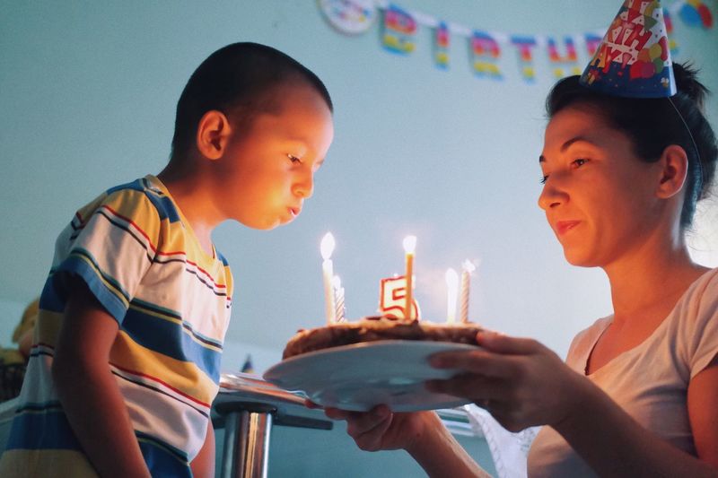 Boy blowing birthday candles with mother at home
