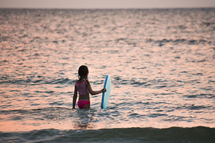 Rear view of woman standing in sea with surfboard