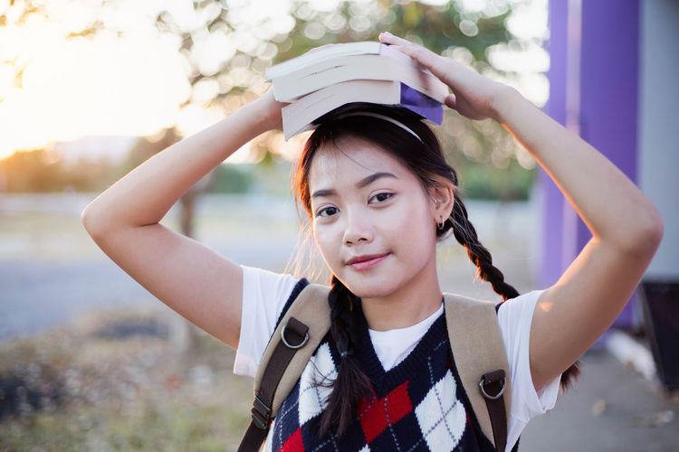 Portrait of smiling young woman holding book on head standing outdoors