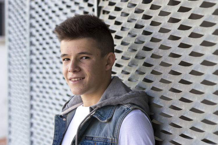 Portrait of teenage boy smiling while standing against metal wall