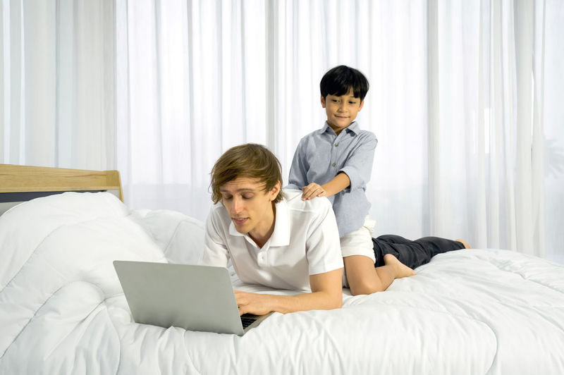 Full length of boy using mobile phone while sitting on bed