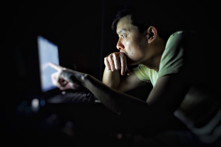 Side view of man using laptop in darkroom