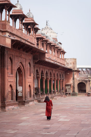 Back view of unrecognizable woman walking barefoot in weathered courtyard of ancient jama masjid building with ornamental arches while visiting agra in uttar pradesh, india