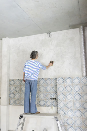 Woman standing on table scrubbing wall at new home