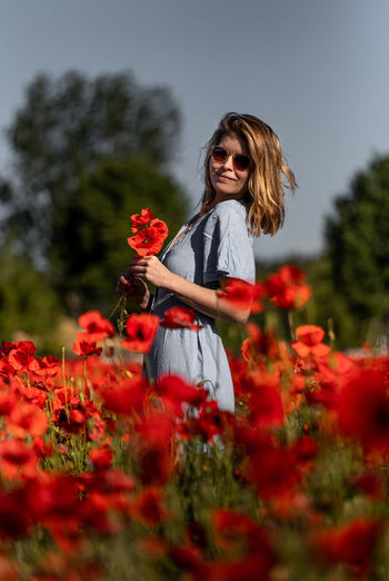 Woman standing by red flower on field