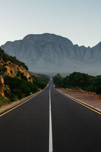 Empty road leading towards mountains against sky.