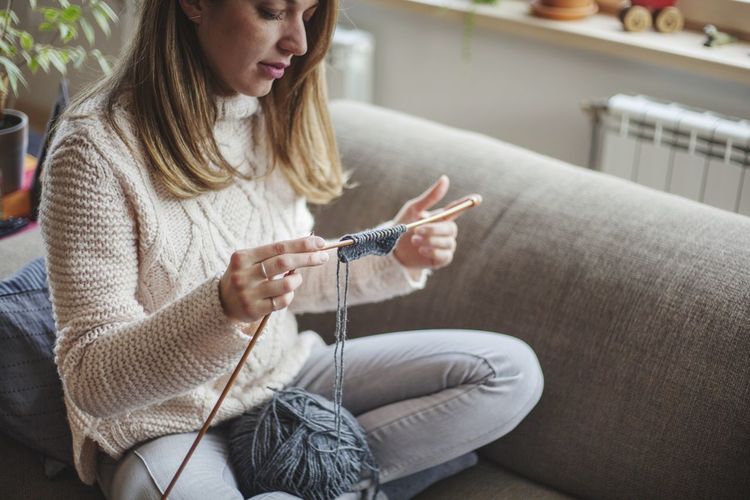 Mid adult woman knitting while sitting on sofa at home