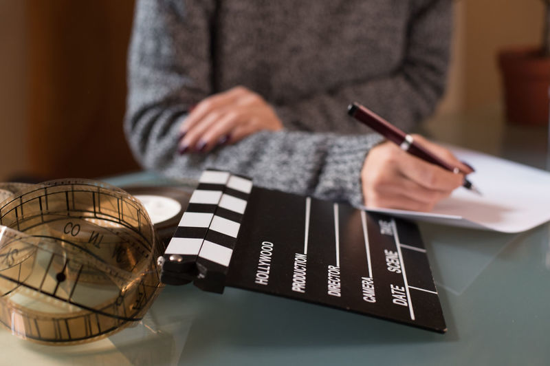 Midsection of woman writing on paper by film slate and reel at table