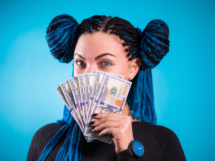 Close-up of young woman holding currency against colored background
