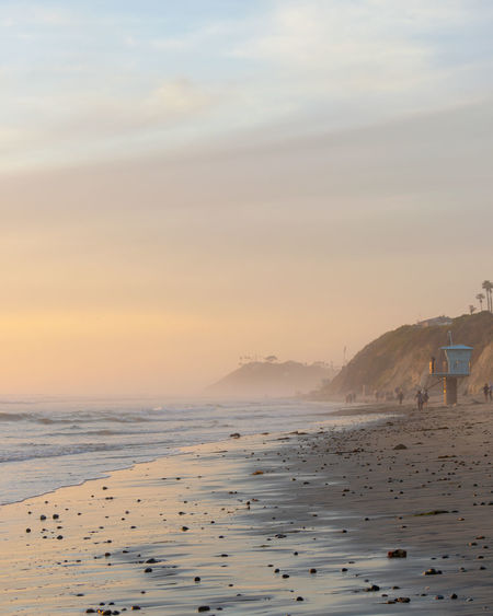 Hazy coastline in san diego during sunset with lifeguard tower and people walking along the beach