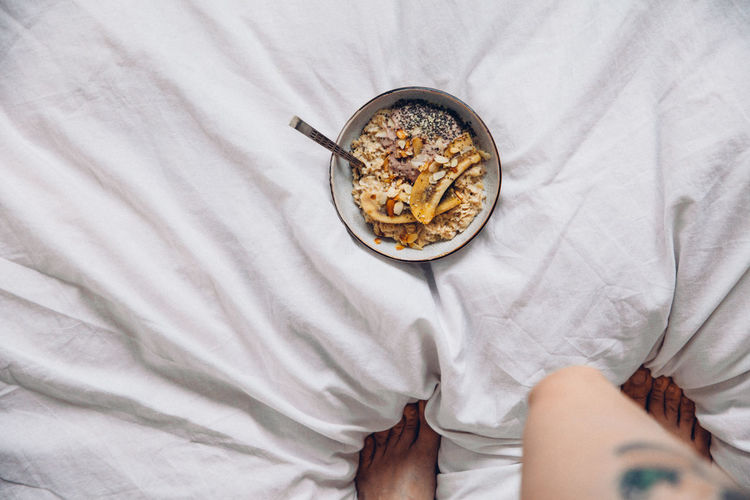 Low section of woman standing by granola bowl on bed