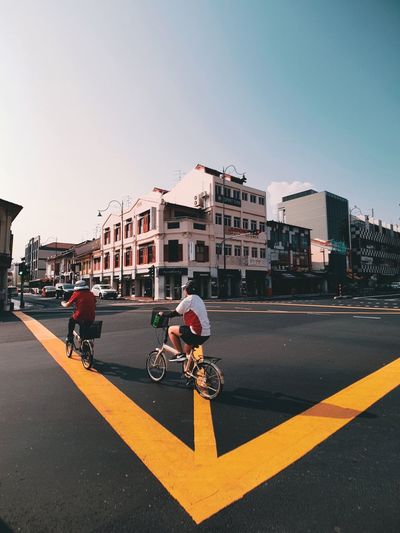 People riding bicycle on road against buildings in city