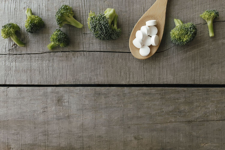 Vitamin or medicine capsules, broccoli on wooden spoon on wooden background. vitamin pills