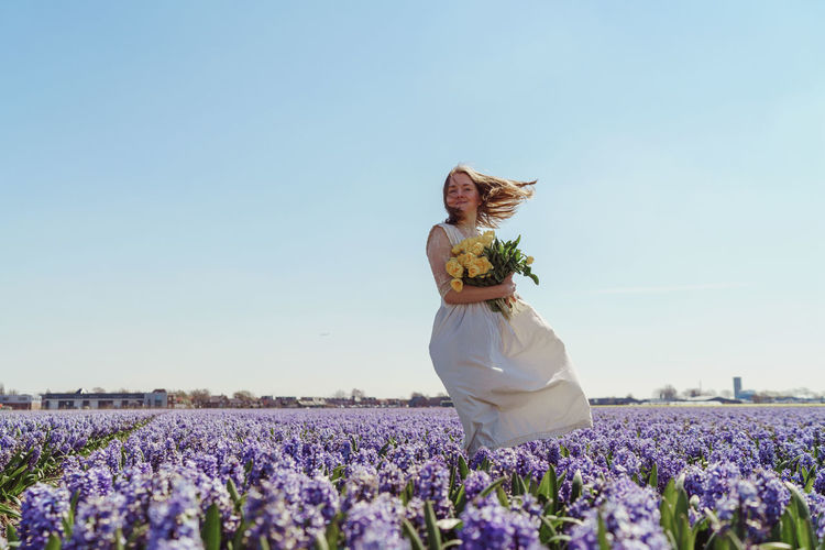 Rear view of woman with flowers on field against clear sky