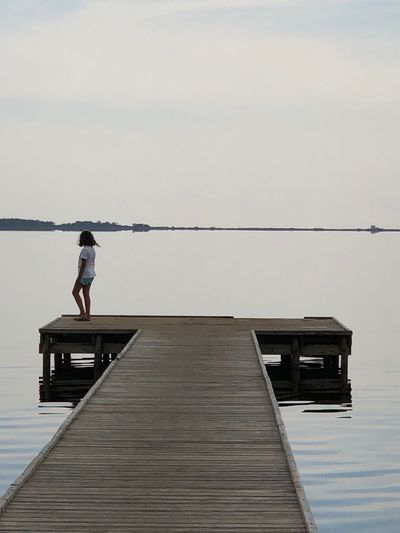 Girl standing on pier by lake against sky