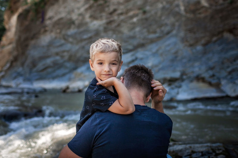 Like father like son. middle aged father embracing cute little son on the bank of river