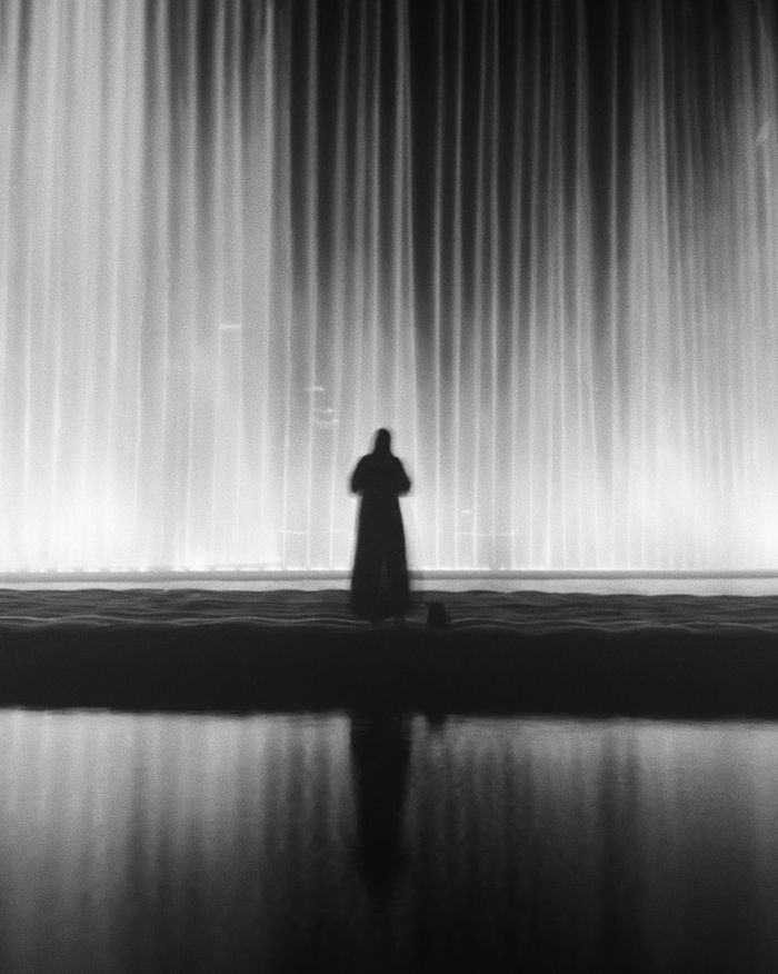 Rear view of silhouette standing against fountain at night
