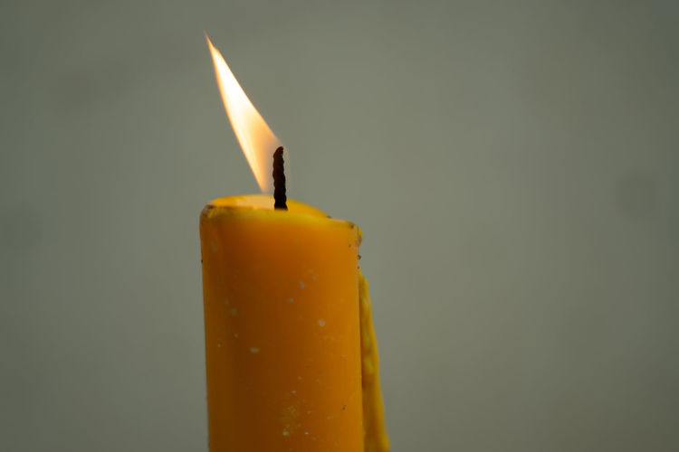 Close-up of lit candle against yellow background