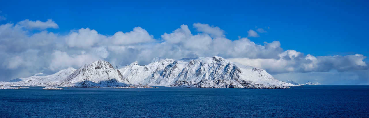 Panoramic view of snowcapped mountains by sea against blue sky
