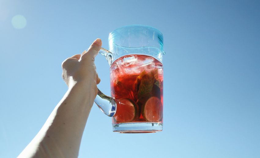 Cropped image of person holding drink against clear blue sky on sunny day