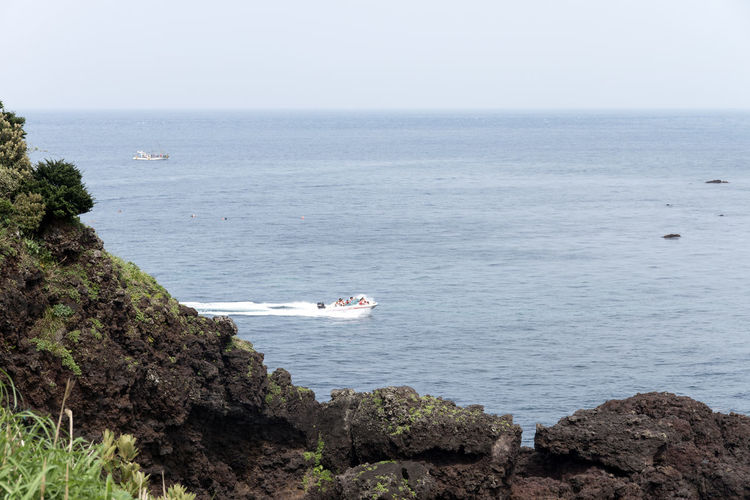 Scenic view of rocks by sea with jet boat at seongsan ilchulbong