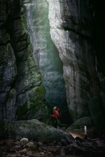A man while inspecting a gorge, illuminated from above and surrounded by millenary rocks.