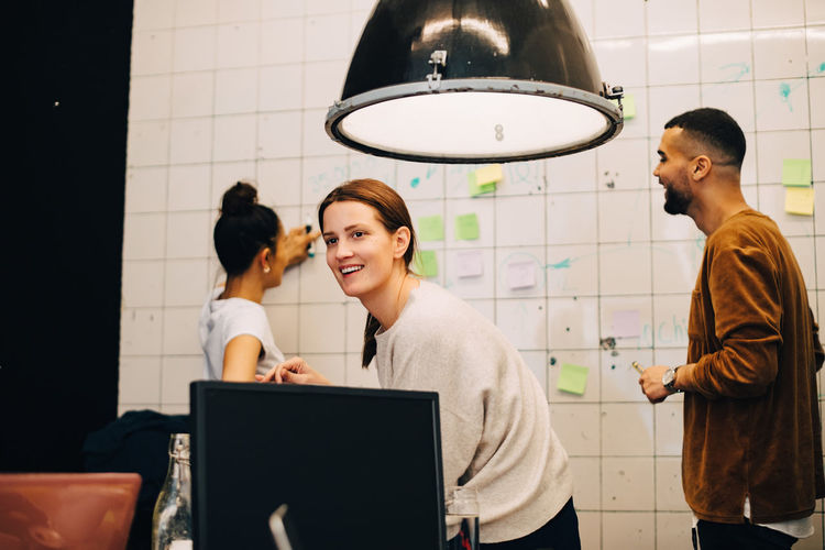 Smiling young businesswoman looking away while hackers planning over wall at small office