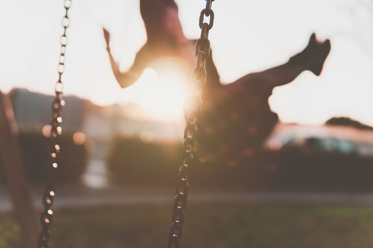 Silhouette person sitting on swing during sunset